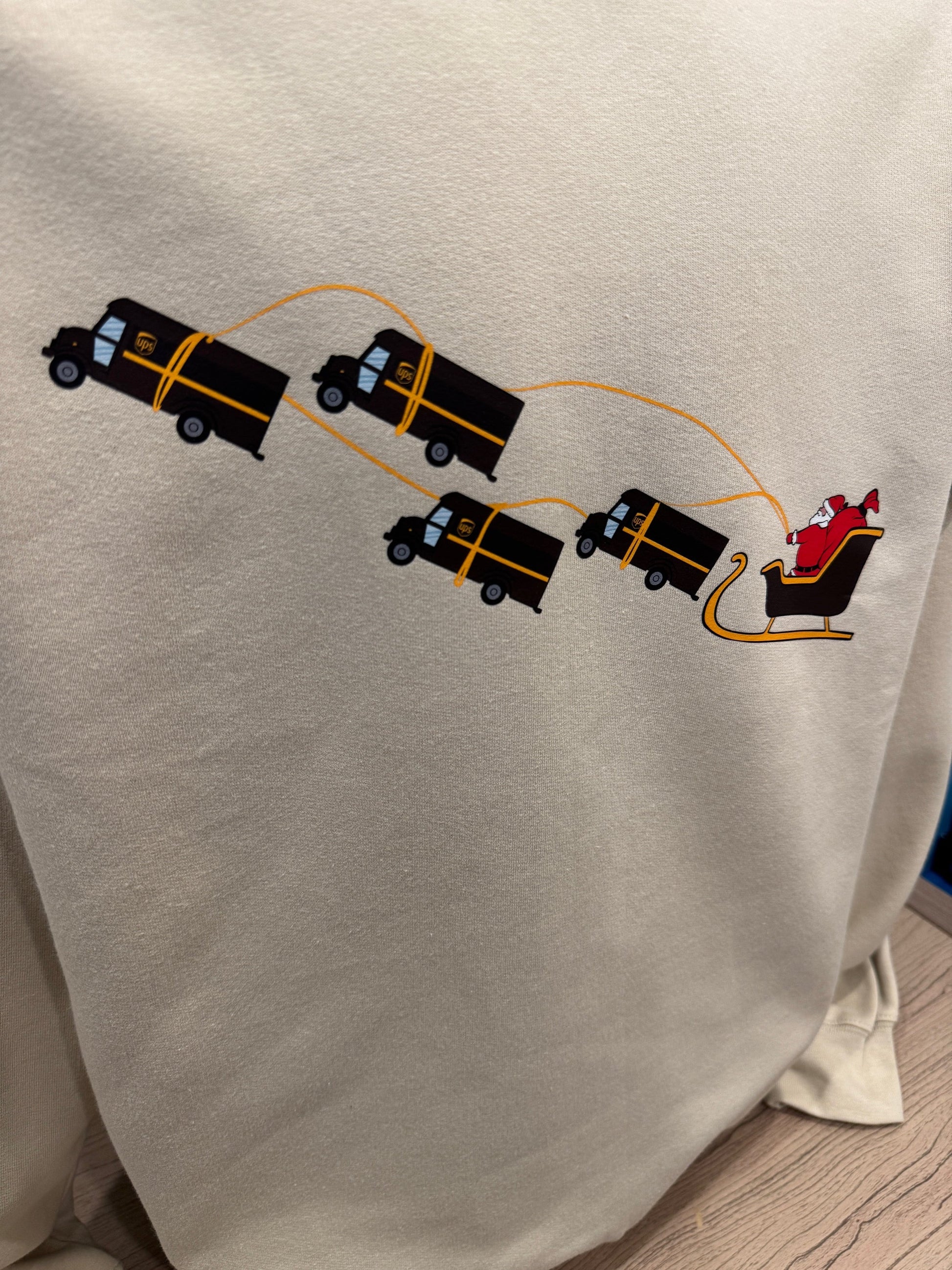 UPS Santa Peak Season Christmas crewneck sweater with Santa in a sleigh pulled by UPS trucks, screen-printed on soft, breathable fabric.
