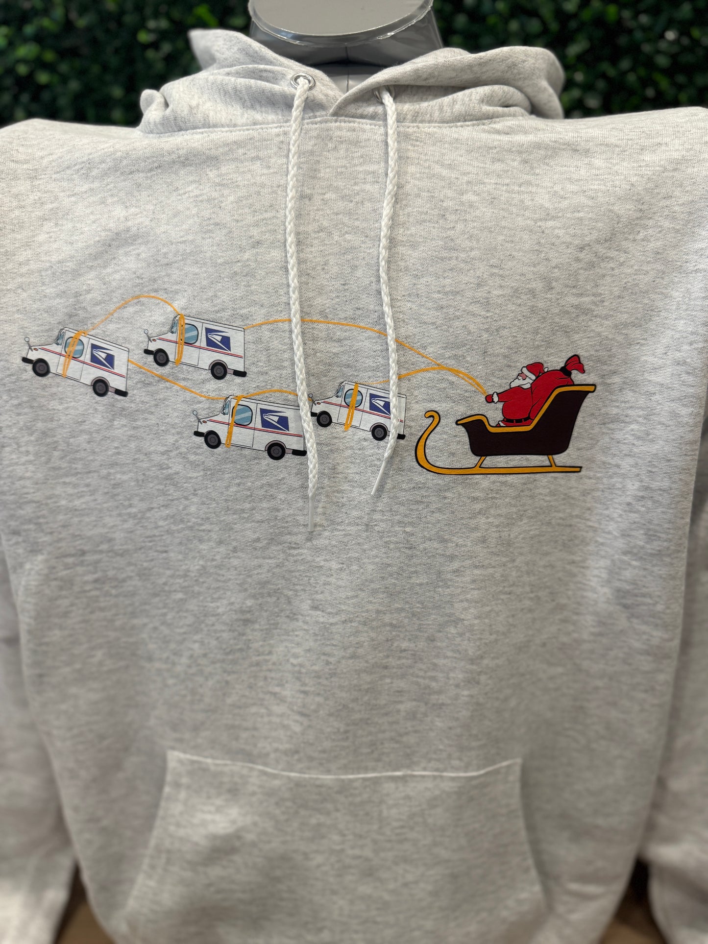 Gray hoodie with printed graphics of Santa Claus USPS Trucks in a sleigh and delivery trucks. Peak Season Gift Postal Worker