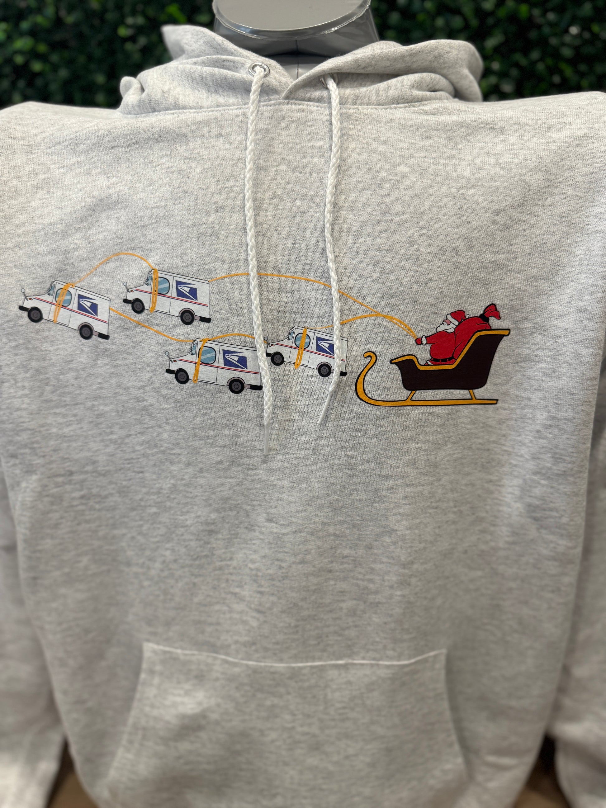 Gray hoodie with printed graphics of Santa Claus USPS Trucks in a sleigh and delivery trucks. Peak Season Gift Postal Worker